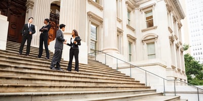 Four well dressed government professionals in discussion on the exterior steps of a building