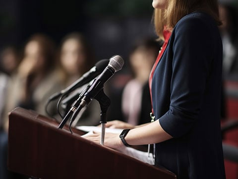 Close up of unrecognizable female politician in rings standing at rostrum with microphones
