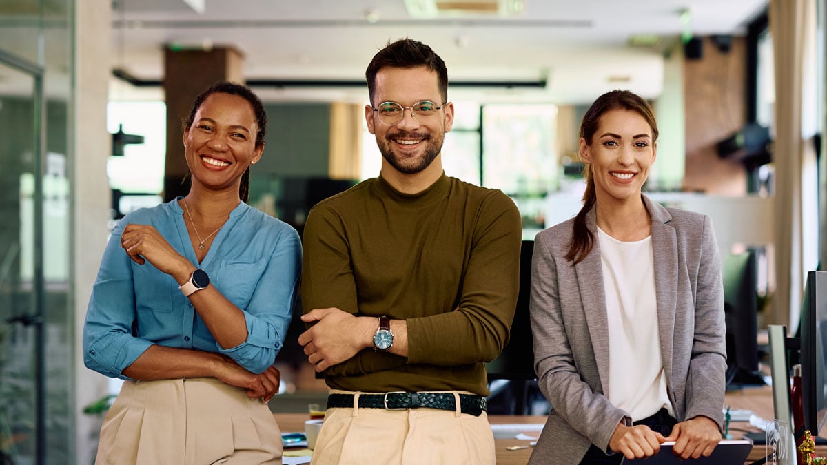 three coworkers smiling at camera in an office